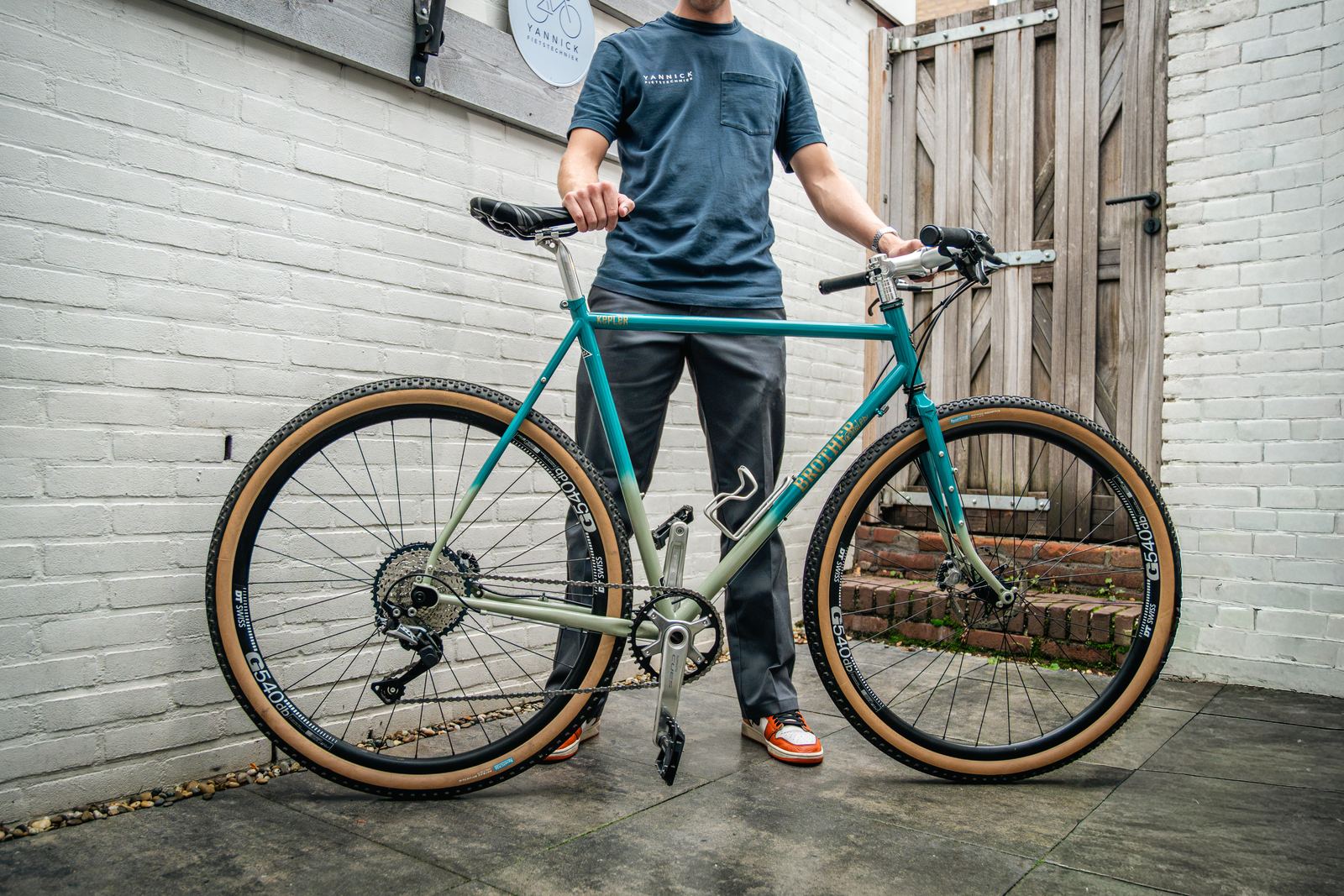 Gravelbike voor de werkplaats onder het bord van Yannick Fietstechniek